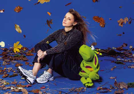 Capucine Duchamp assise au milieu de feuilles d'automne avec Eliott, sa marionnette de dragon vert