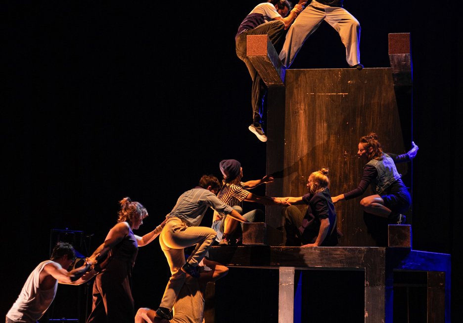 Les acrobates s'entraident pour escalader une haute structure en bois sur scène